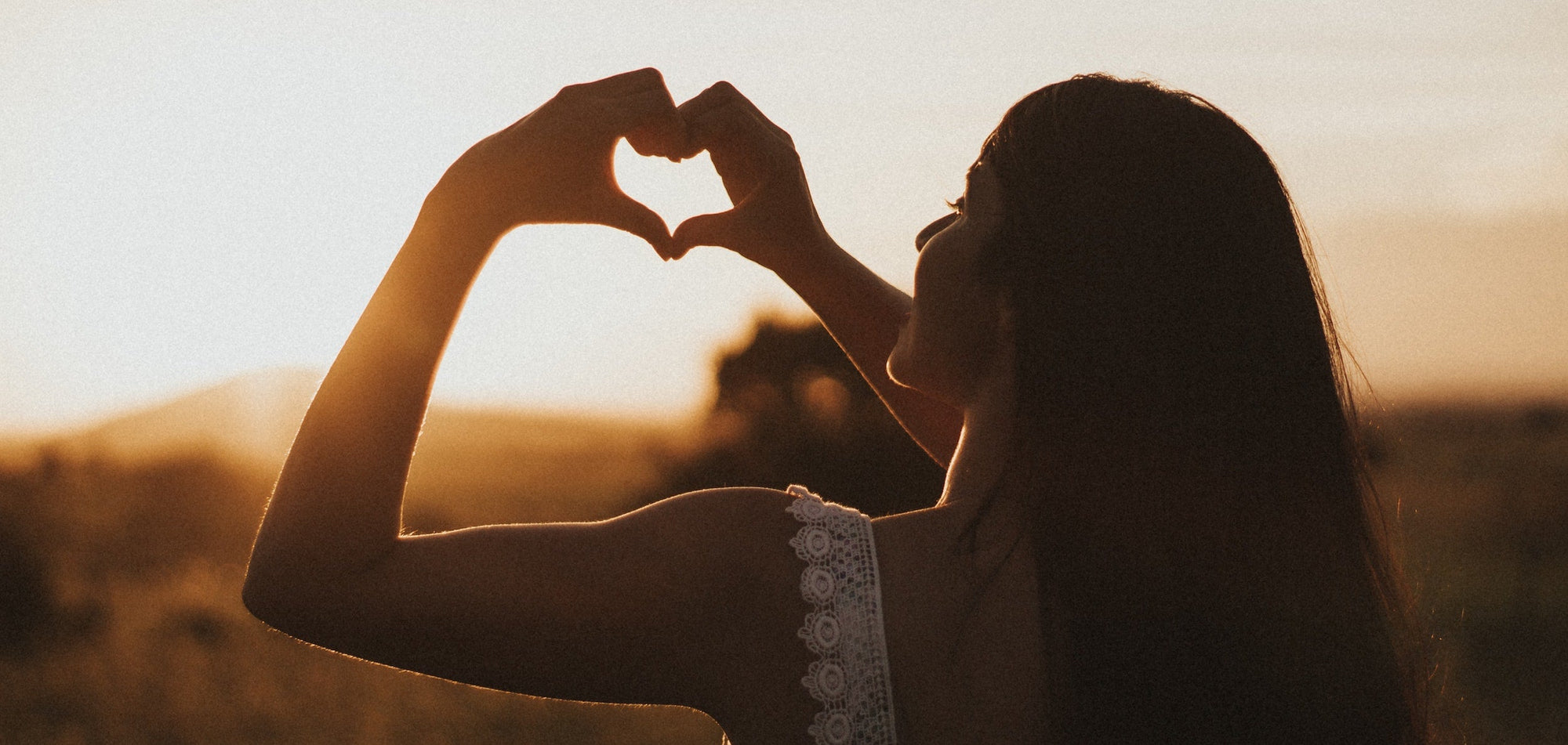 Woman making heart with hands at sunset