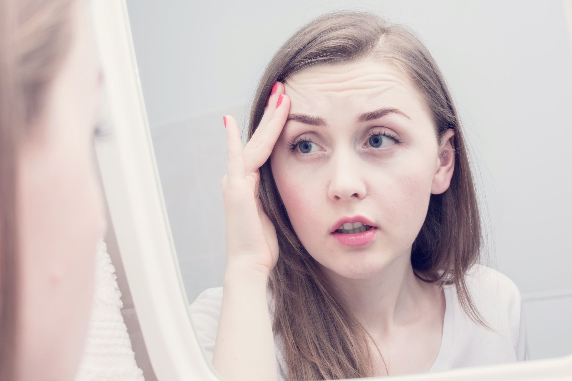 Young woman examines skin complexion in mirror