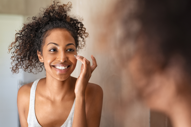 Woman with dark skin smiling while doing her skin care regimen 