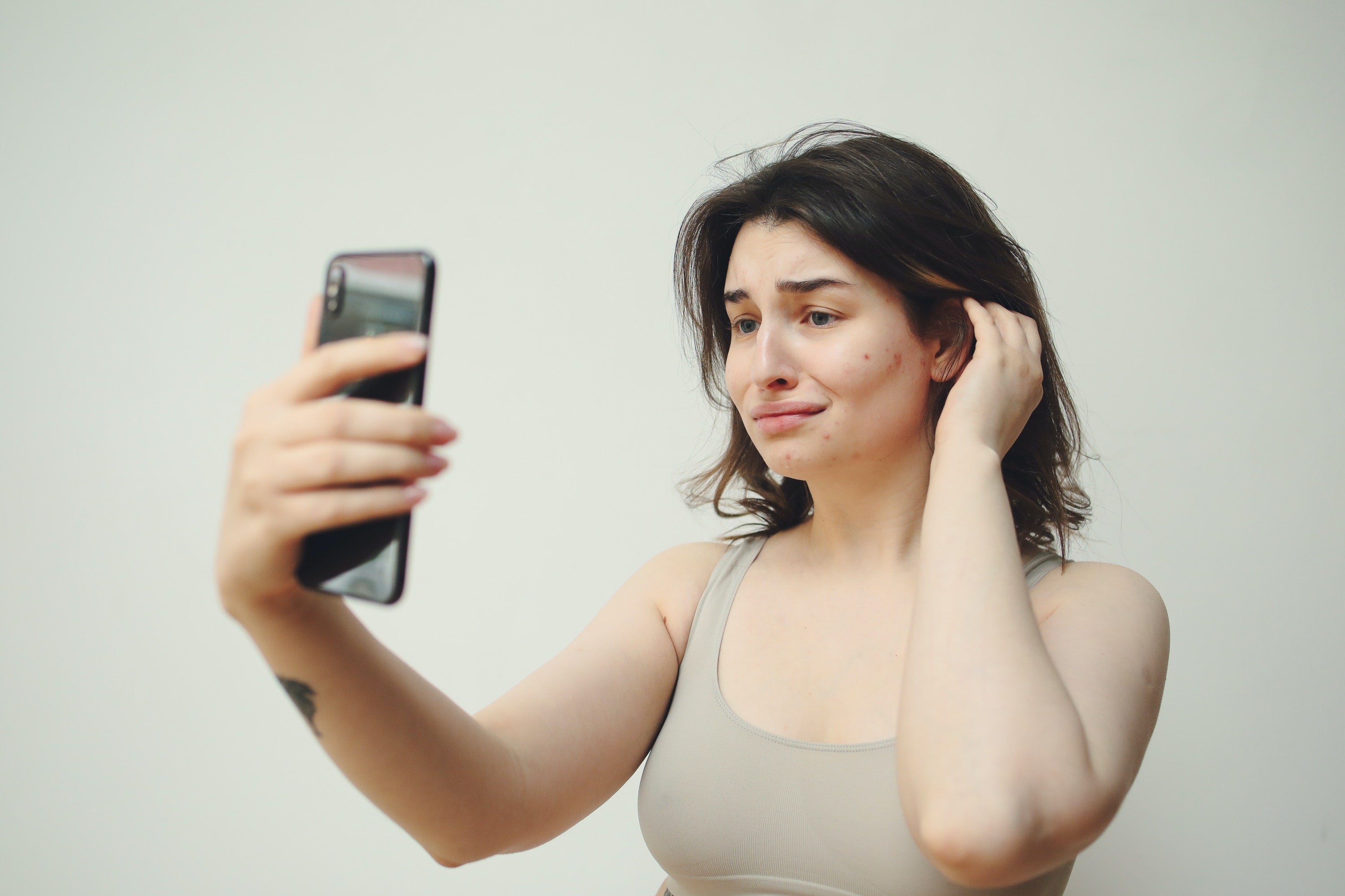 A woman holding a phone up. She looks unhappy with her appearance.