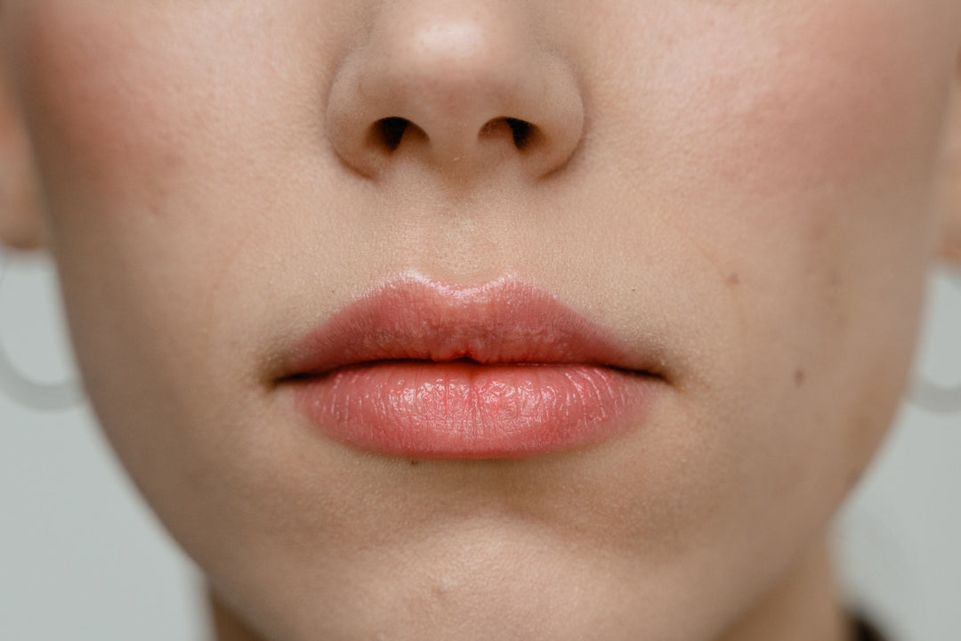 A woman's closed mouth with a faint coral shade of lipstick