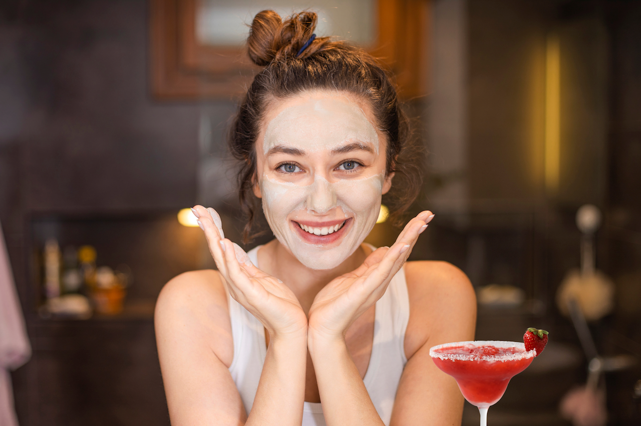 Woman doing skincare routine while drinking cocktail