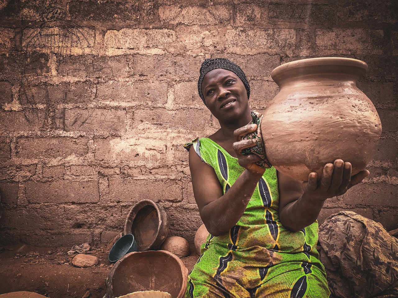 An African woman is holding a clay pot. She is smiling a little.