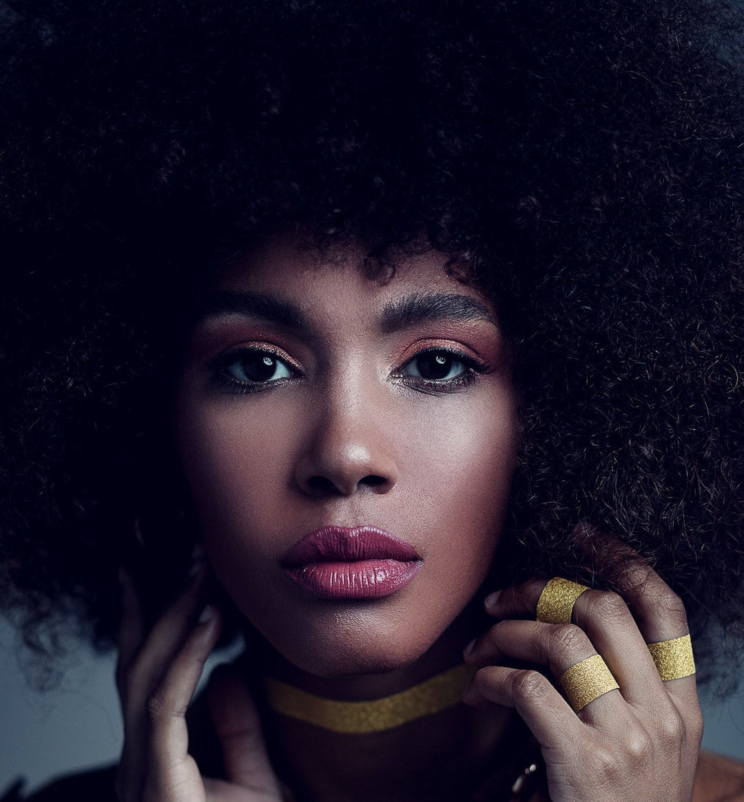A Black woman wearing her natural hair while wearing make-up and gold rings